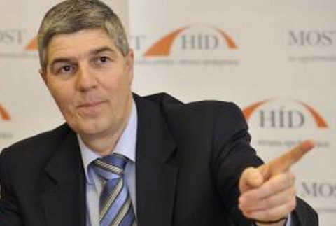 Béla Bugár vpredu, logo za ním, ukazuje prstom