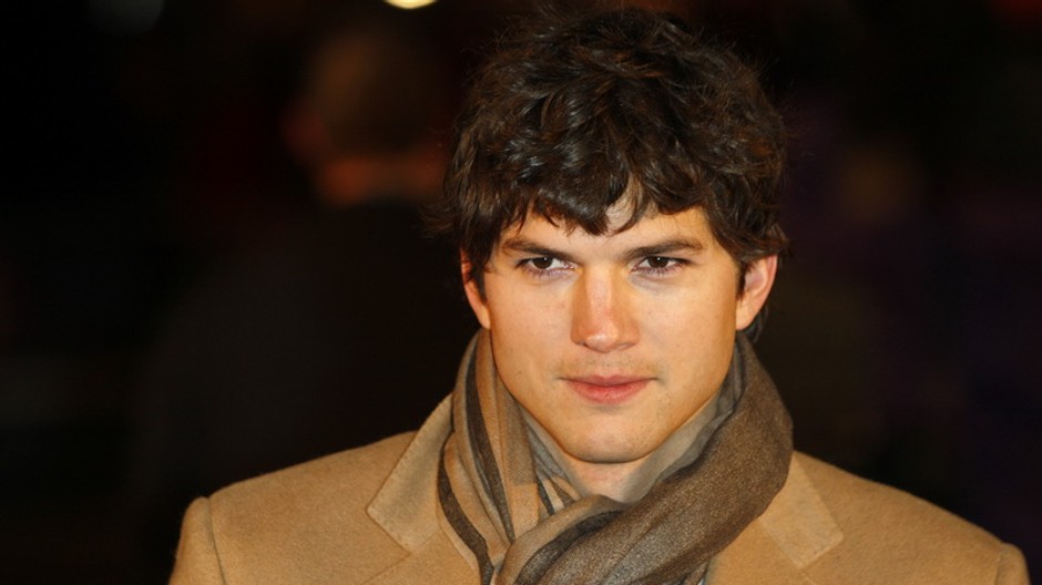Ashton Kutcher v kabáte a šále, busta, premrznutý úsmev