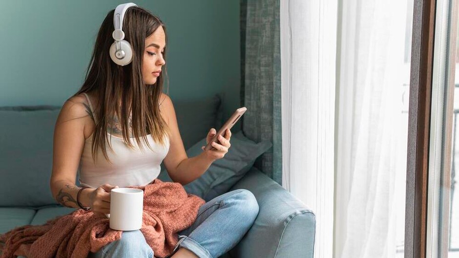 woman-using-smartphone-with-headphones-home-while-having-coffee
