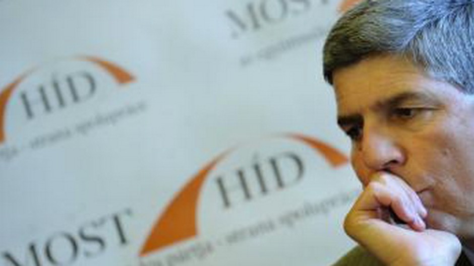 bela bugar, zamysleny, za nim logo Most-Híd