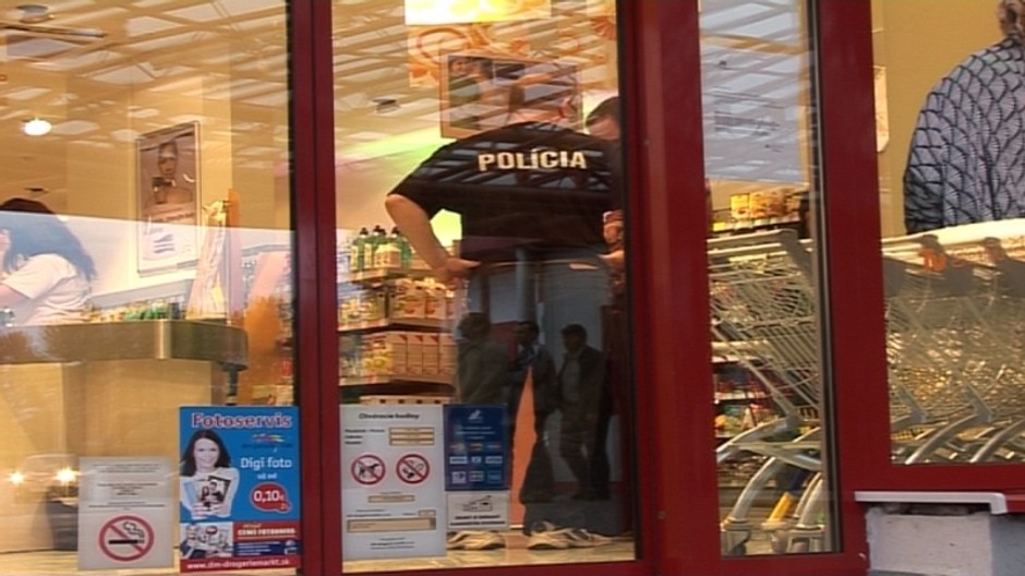 obchod zvonku, sklenene dvere, za nimi policajt