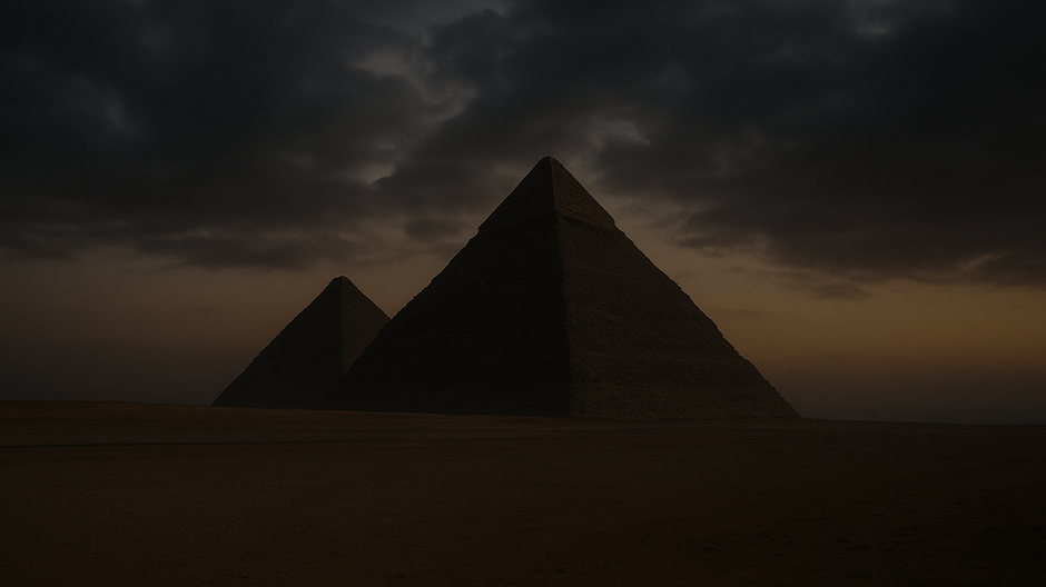Veľké pyramídy v Gíze zachytené pri západe slnka, siluety monumentálnych stavieb kontrastujú s dramatickou oblohou a púštnou krajinou.