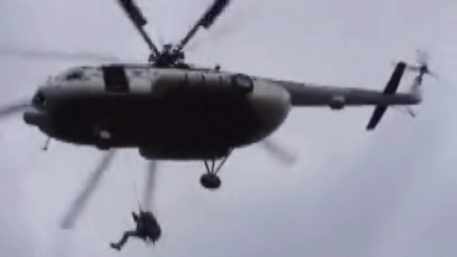 Vrtuľník vo vzduchu, muž zlieza po lane na zem