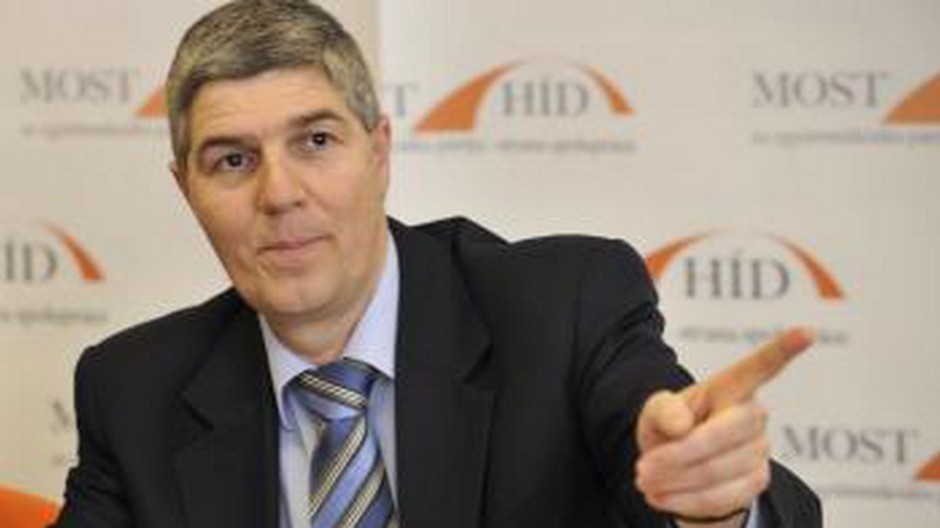 Béla Bugár vpredu, logo za ním, ukazuje prstom