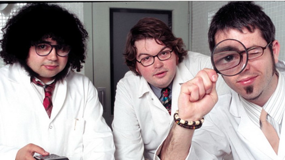 traja studenti v bielych plastoch a s lupou